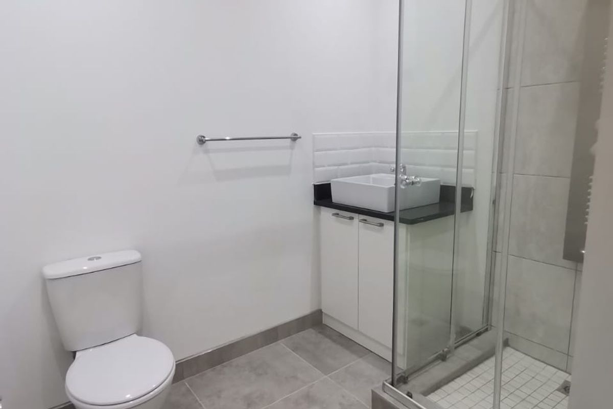 A clean, modern bathroom featuring a glass-enclosed shower, a vanity with a vessel sink, and neutral grey floor tiles.