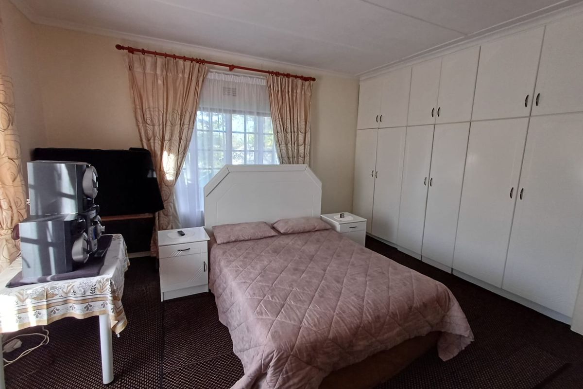 A functional bedroom featuring extensive floor-to-ceiling built-in cupboards and natural light through a window with curtain rails.