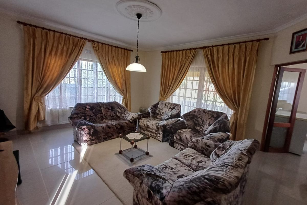A spacious living room featuring tiled flooring, decorative ceiling rose with pendant lighting, and large windows fitted with security bars.