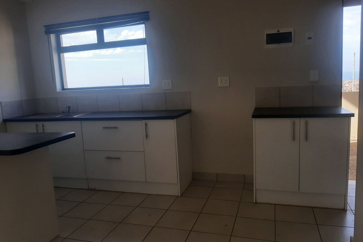 A clean, empty kitchen featuring white built-in cabinetry, dark laminate countertops, tiled flooring, and a tiled backsplash with a window view.