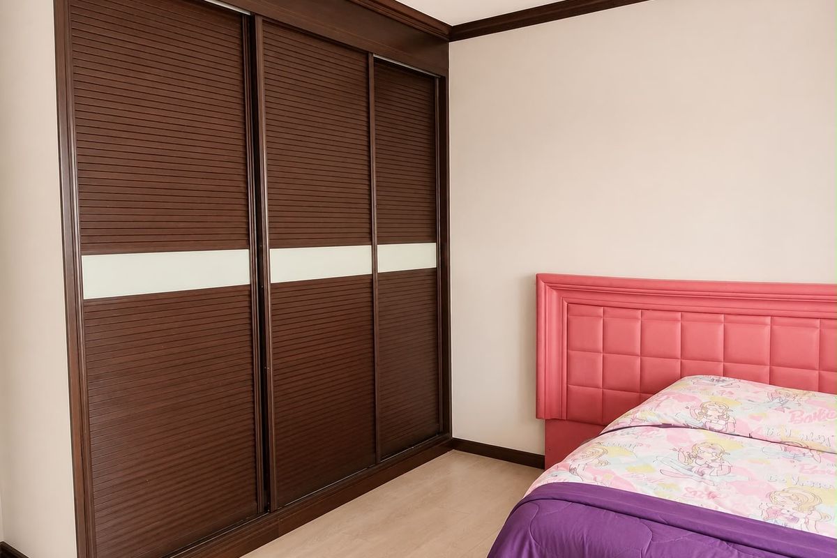 A bedroom featuring a large, dark wood built-in sliding door wardrobe with white accent panels and crown molding details.