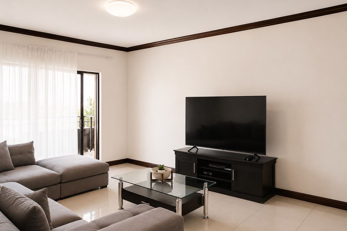 A bright and well-maintained living room featuring neutral tiled flooring, dark crown molding, and a sliding glass door providing access to the balcony.