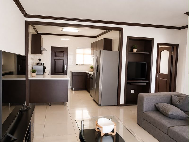 An open-plan living and kitchen area featuring modern dark cabinetry, tiled flooring, and built-in recessed shelving, creating a cohesive and functional living space.