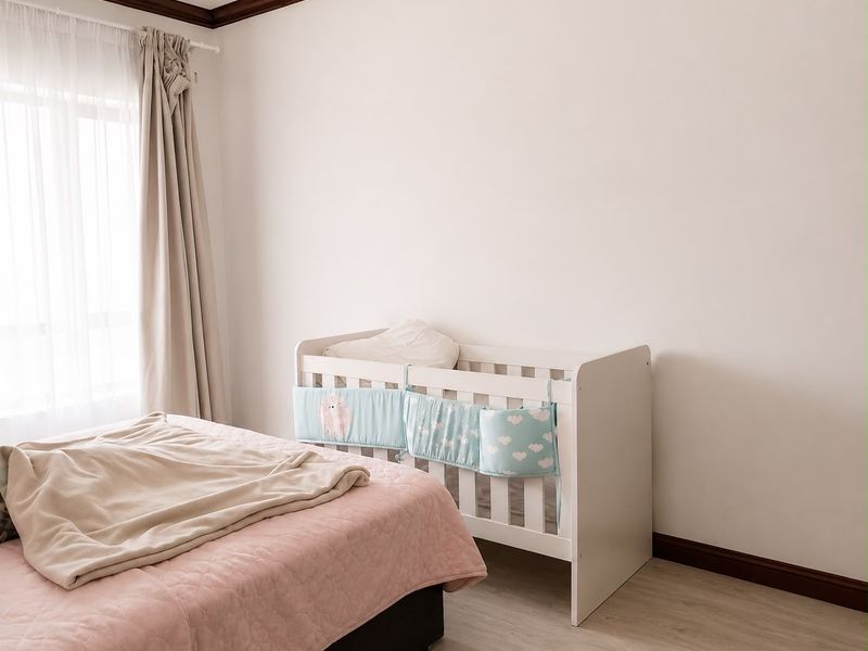 A bright and well-maintained bedroom featuring light-toned laminate flooring, dark timber crown molding, and matching skirting boards.