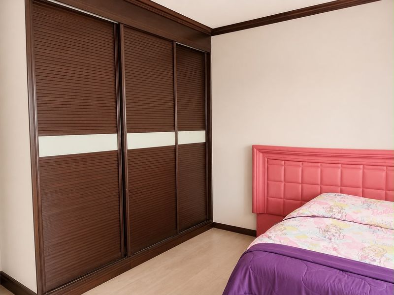 A bedroom featuring a large, dark wood built-in sliding door wardrobe with white accent panels and crown molding details.