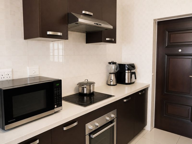 A modern kitchen featuring dark wood cabinetry, stone countertops, a built-in oven, electric hob, and a stainless steel extractor fan.