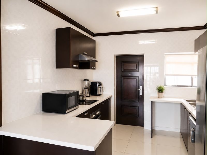 A modern kitchen featuring dark wood cabinetry, stone countertops, integrated appliances, and tiled finishes, providing a clean and functional workspace.