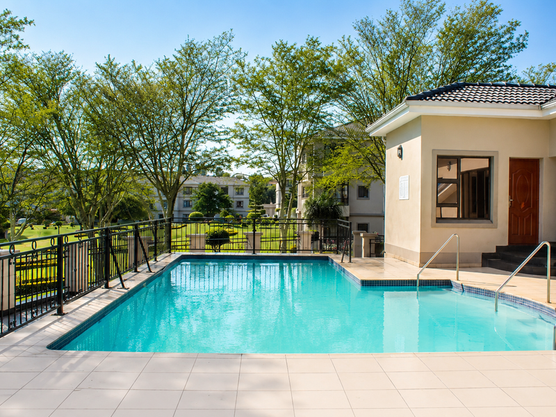 A well-maintained outdoor swimming pool area featuring a tiled deck, metal safety railings, and access to the adjacent building structure.