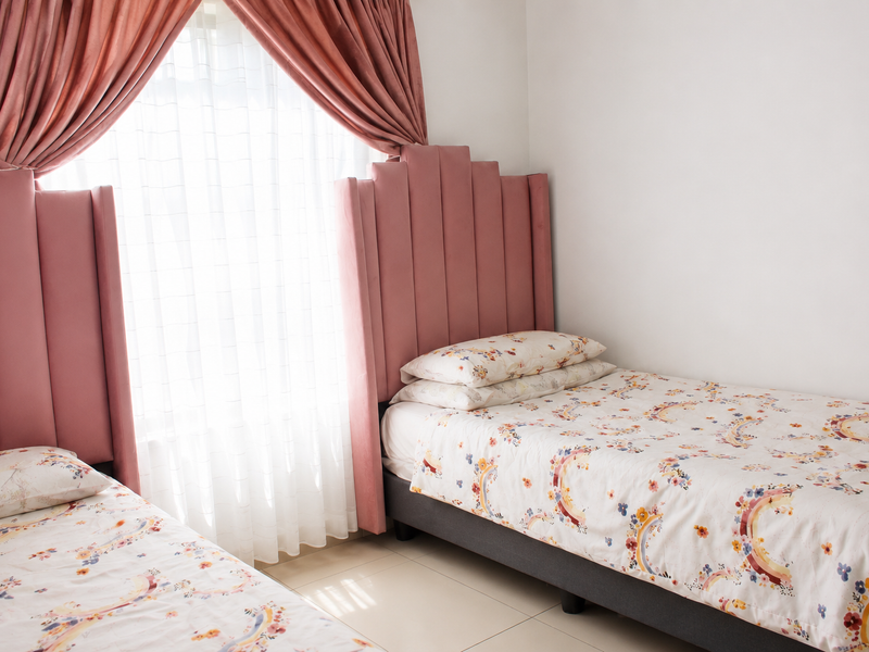 A bright bedroom featuring tiled flooring and large windows with elegant floor-to-ceiling curtains, providing a clean and well-maintained living space.