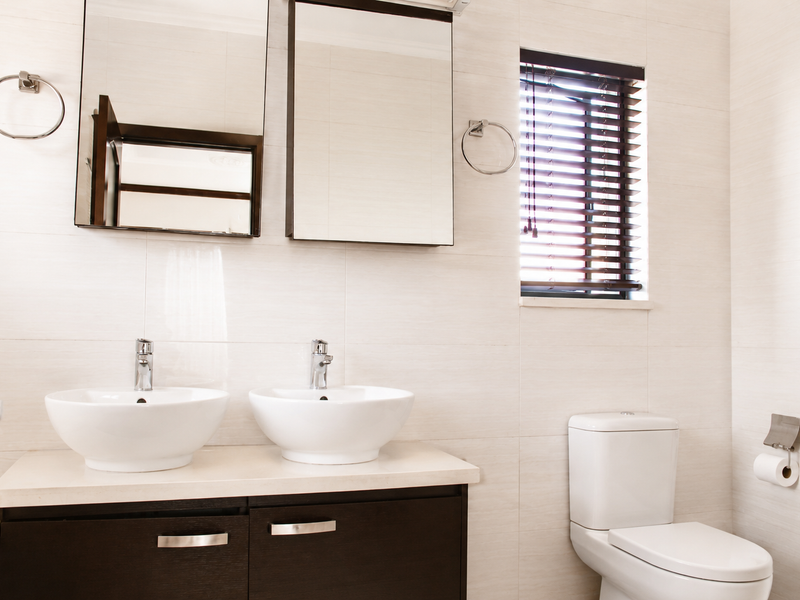 Modern bathroom featuring a double vanity with vessel sinks, chrome fixtures, wall-mounted mirrors, and a toilet, finished with neutral wall tiling.