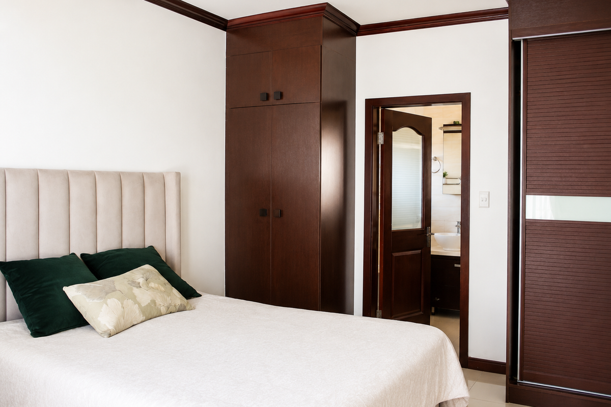 A well-maintained bedroom featuring dark wood built-in cabinetry, crown molding, and direct access to an en-suite bathroom with tiled flooring throughout.