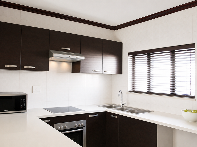 Modern kitchen featuring dark wood cabinetry, white stone countertops, stainless steel appliances, and a tiled backsplash with natural light from the window.