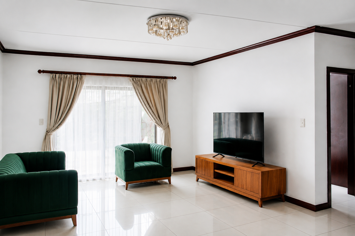 A bright and well-maintained living room featuring polished tile flooring, elegant crown molding, and a sliding glass door providing natural light.