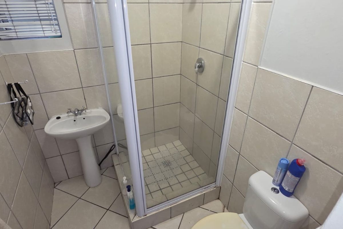 A functional bathroom featuring a pedestal washbasin, a glass-enclosed shower, and tiled finishes throughout.