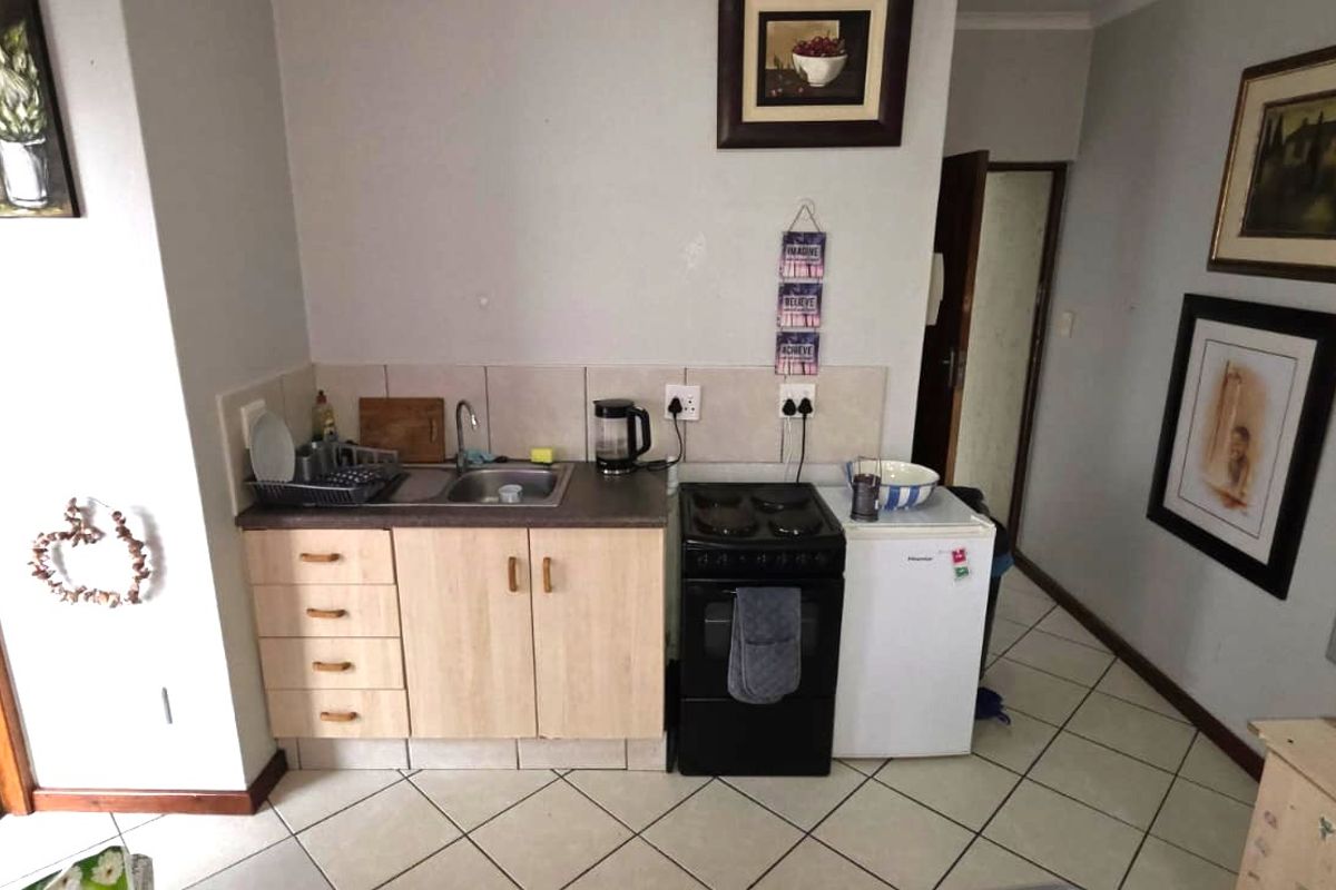 Compact kitchen area featuring laminate cabinetry, a stainless steel sink, tiled backsplash, and a freestanding stove with ceramic floor tiles.