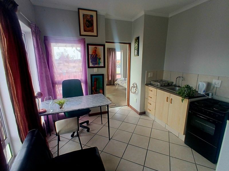 An open-plan living and kitchen area featuring tiled flooring, functional cabinetry, and a built-in stove, with direct access to an adjacent bedroom.