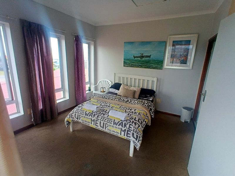 A bedroom featuring carpet flooring and large aluminium-framed windows that provide natural light.