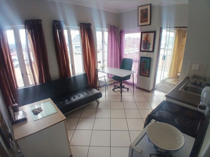 Open-plan living area featuring ceramic tiled flooring, a compact kitchen corner with a sink and electric stove, and large windows providing natural light.