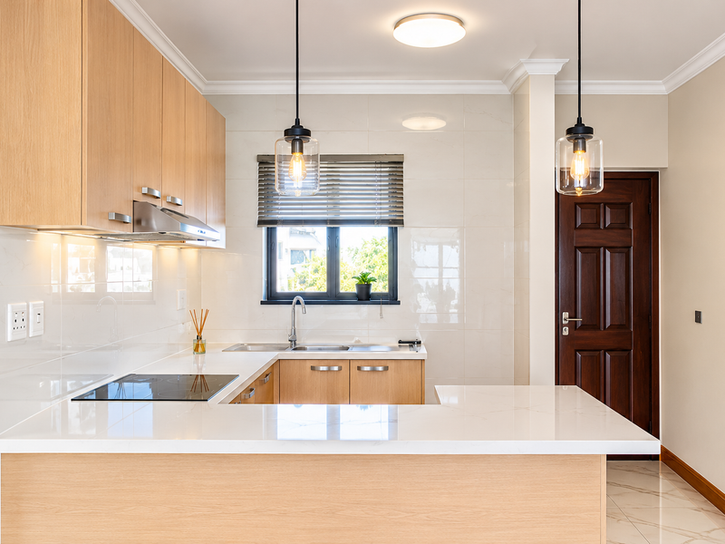 Modern kitchen featuring light wood cabinetry, quartz countertops, integrated induction hob, stainless steel extractor, and elegant pendant lighting in a clean, well-maintained space.