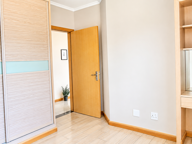 A bright bedroom featuring light timber flooring, a large built-in sliding wardrobe, and a dedicated built-in vanity area with shelving.