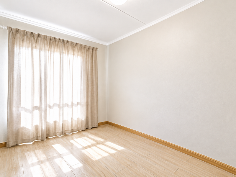 A bright, empty bedroom featuring light-toned laminate flooring, neutral walls, and ceiling cornicing, offering a clean and versatile space.