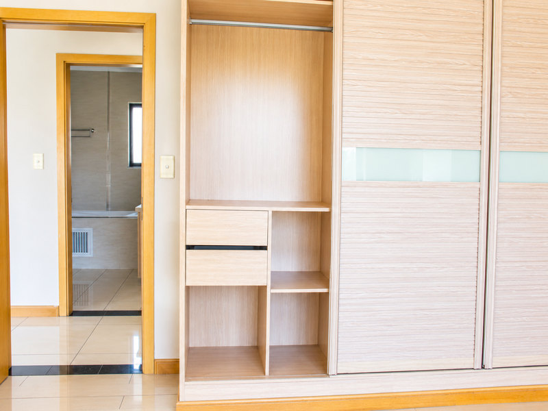A bedroom featuring a large built-in wardrobe with sliding doors and light wood finish, with a view into an adjacent tiled bathroom.
