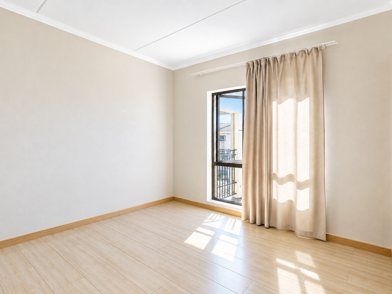 A bright, empty bedroom featuring light-toned laminate flooring, neutral walls, and built-in shelving, offering a clean and versatile space.