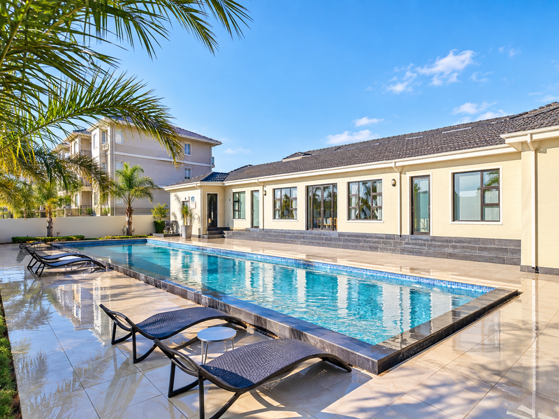 A well-maintained outdoor swimming pool area featuring a tiled deck, modern facade, and direct access to the building through sliding glass doors.