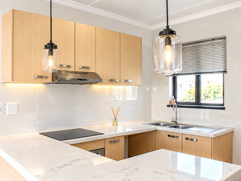 Modern kitchen featuring light oak cabinetry, marble-look quartz countertops, induction hob, stainless steel extractor, and elegant pendant lighting.