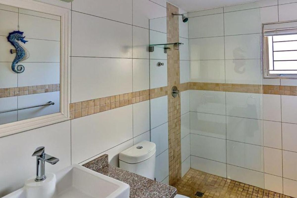 A clean, modern bathroom featuring a glass-enclosed shower, granite vanity countertop, and neutral wall tiling with a decorative mosaic accent border.