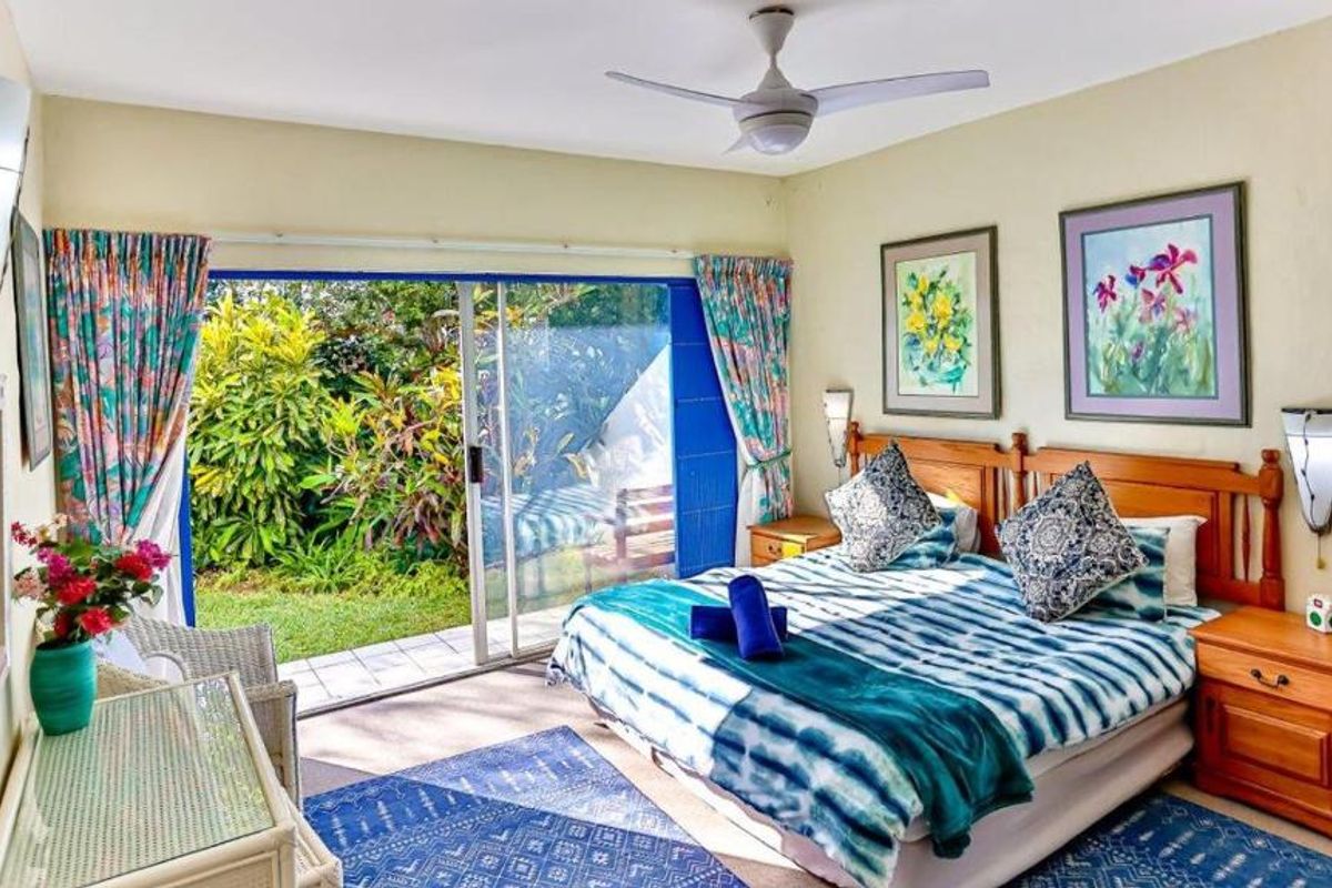 A bedroom featuring a ceiling fan and large sliding glass doors that open directly onto a private garden patio.