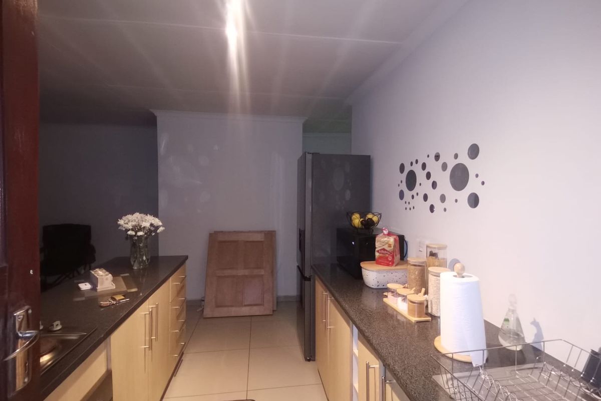 A functional galley-style kitchen featuring light wood cabinetry, dark granite countertops, and tiled flooring, offering a practical layout for daily meal preparation.