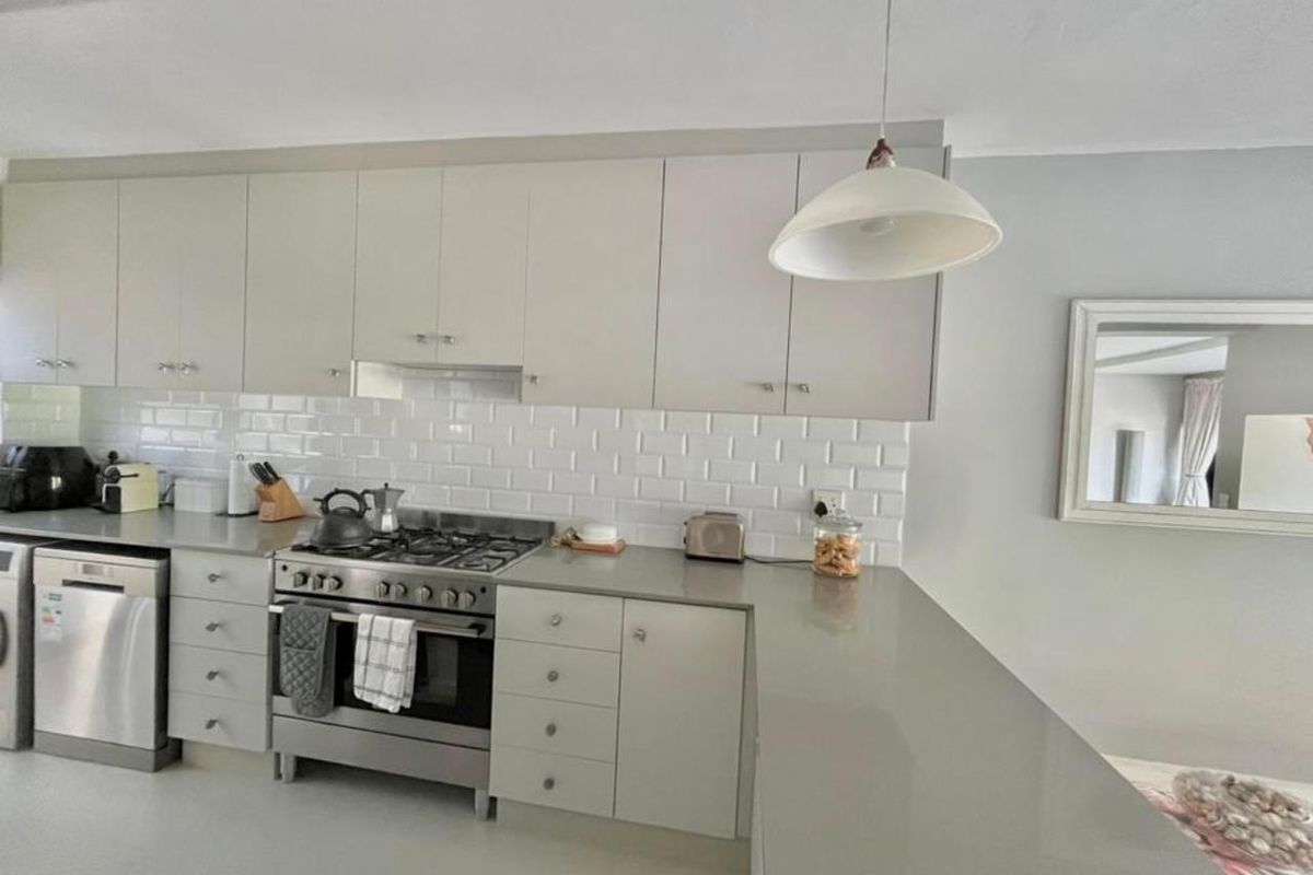 Modern kitchen featuring light grey cabinetry, subway tile backsplash, quartz countertops, and a stainless steel gas stove with integrated extractor fan.