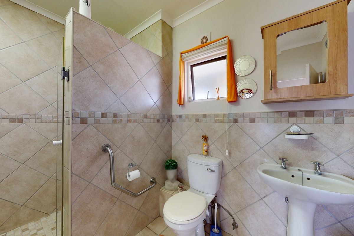 A functional bathroom featuring a walk-in shower with a grab rail, pedestal basin, and wall-mounted medicine cabinet, finished with neutral wall and floor tiles.