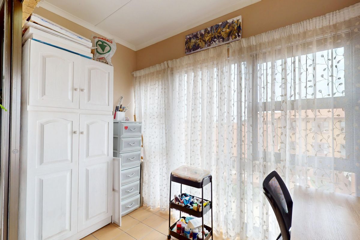 A functional bedroom featuring tiled flooring, a built-in cupboard, and a large window allowing for natural light.