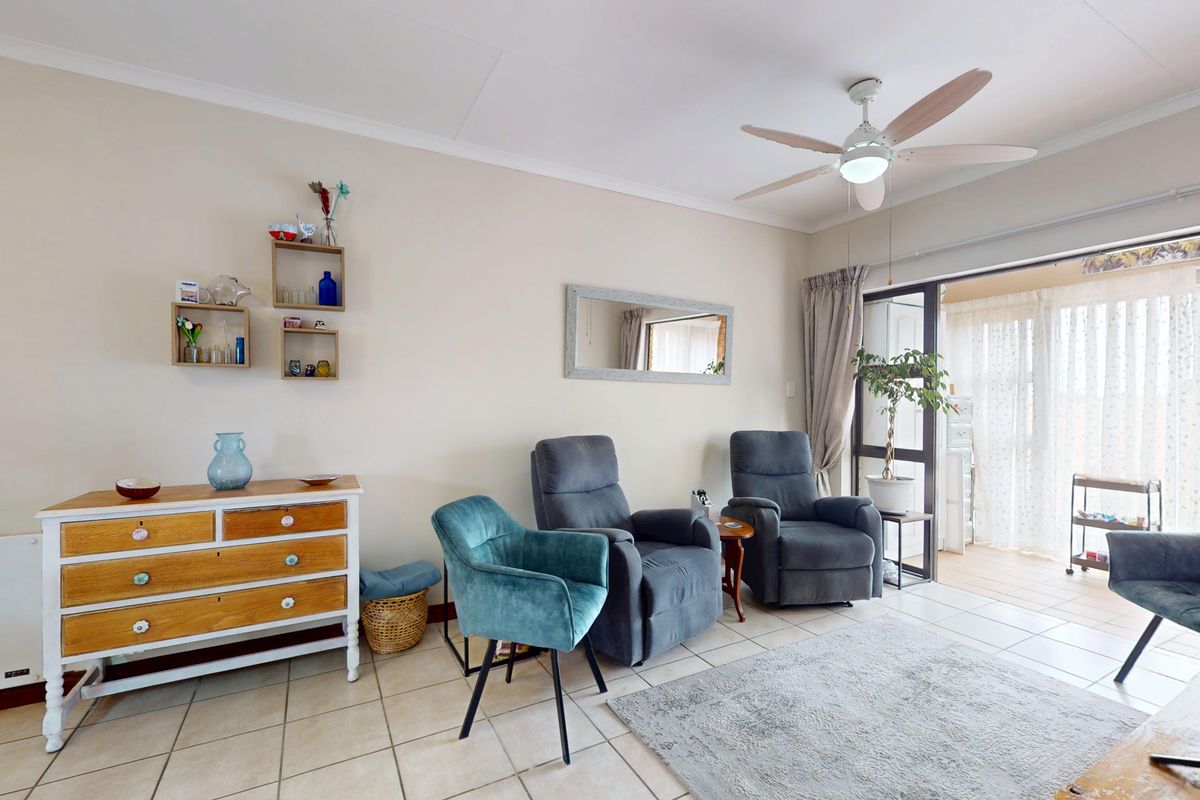 A bright living room featuring tiled flooring, a ceiling fan, and a large sliding glass door providing access to the patio area.