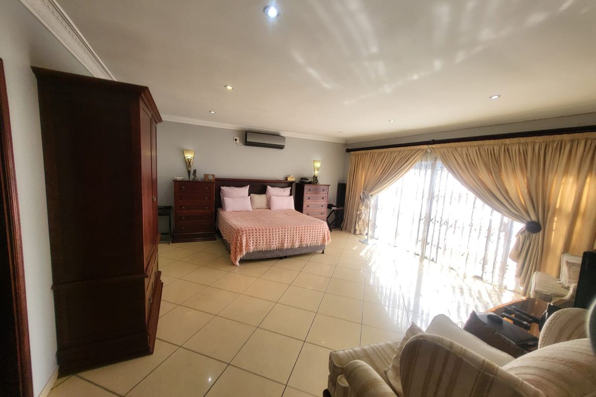 Spacious bedroom featuring large format floor tiles, recessed lighting, wall-mounted air conditioning, and sliding glass doors providing ample natural light.