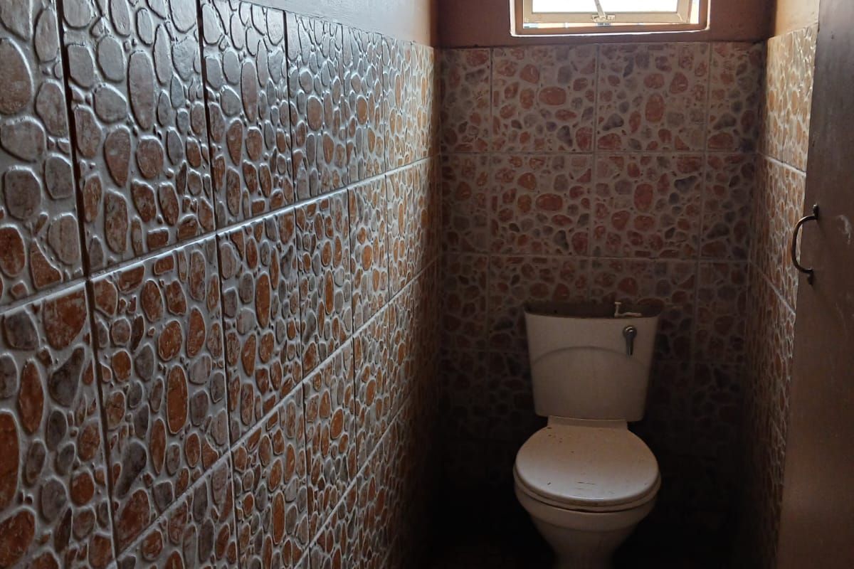 A small, functional bathroom featuring full-height decorative wall tiling, floor tiles, and a single casement window for natural light.