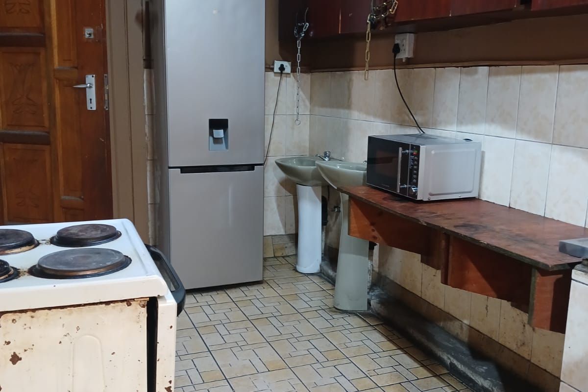 A dated kitchen area featuring wall-mounted cabinetry, pedestal sinks, tiled backsplash, and an electric stove with visible wear on the finishes.
