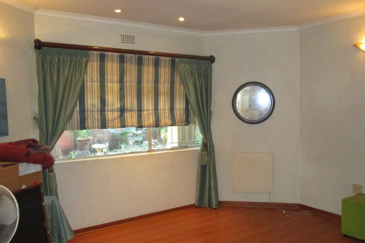 A living room featuring laminate flooring, recessed downlights, wall-mounted sconces, and a built-in wall heater, with a window overlooking the garden.