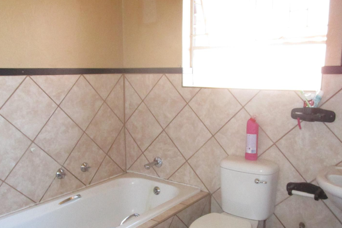 A functional bathroom featuring a built-in bathtub, pedestal washbasin, and toilet with neutral diamond-patterned wall tiling.