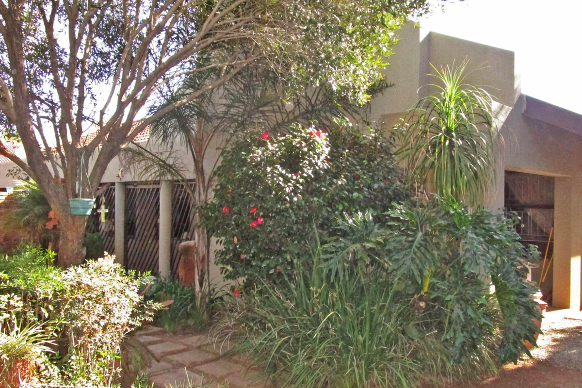 Rear view of the property featuring a landscaped garden, paved walkway, and sliding glass door access to the home.