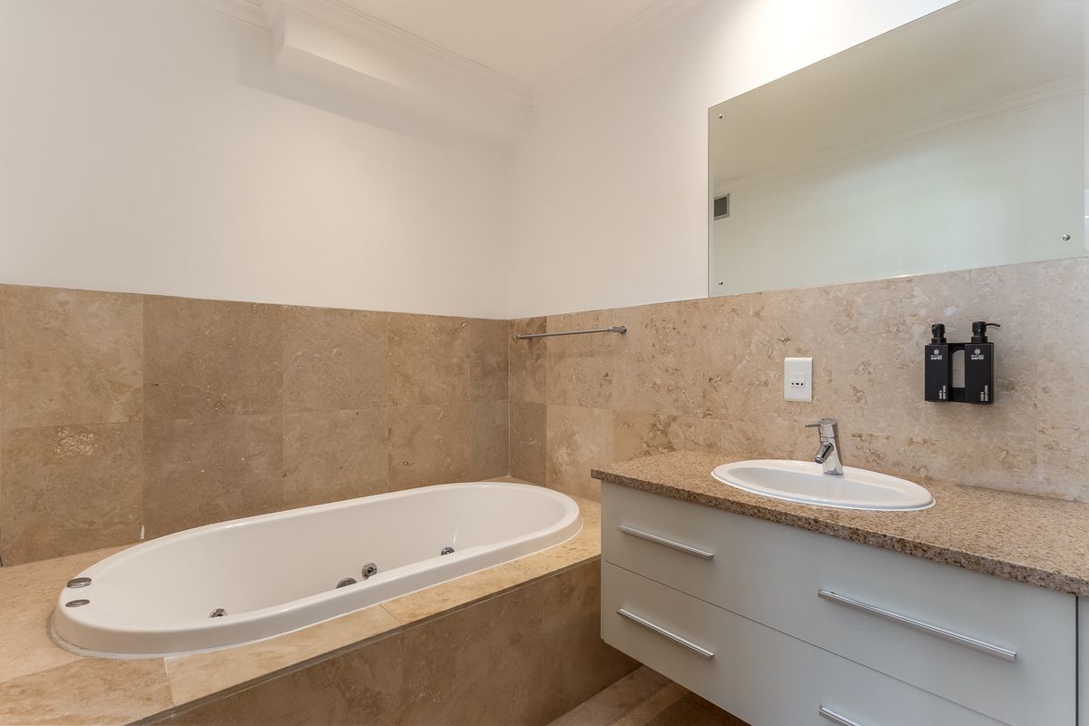 A well-maintained bathroom featuring a built-in jetted bathtub, stone-tiled surround, and a modern vanity with an integrated basin and wall-mounted mirror.