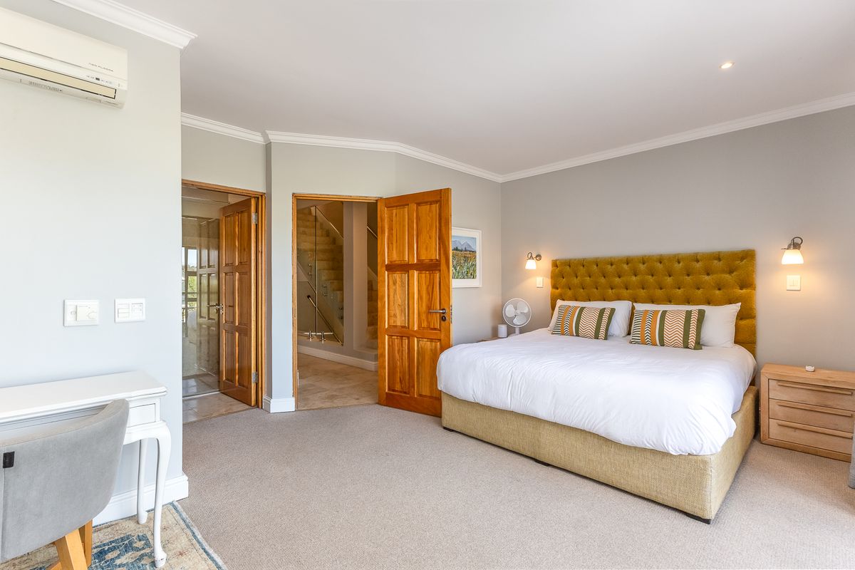 Spacious bedroom featuring neutral carpeting, crown molding, wall-mounted air conditioning unit, and direct access to an en-suite bathroom and hallway.