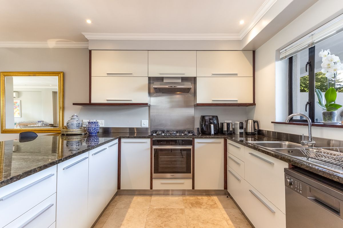 Modern kitchen featuring sleek white cabinetry, dark granite countertops, stainless steel gas hob, built-in oven, extractor fan, and a double sink with tiled flooring.