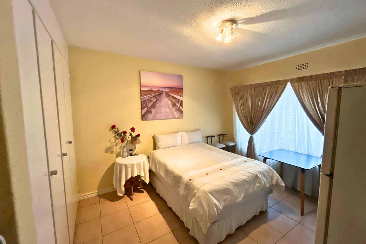 A bedroom featuring tiled flooring, built-in cupboards, and a ceiling light fixture, offering a functional space with potential for cosmetic updates.