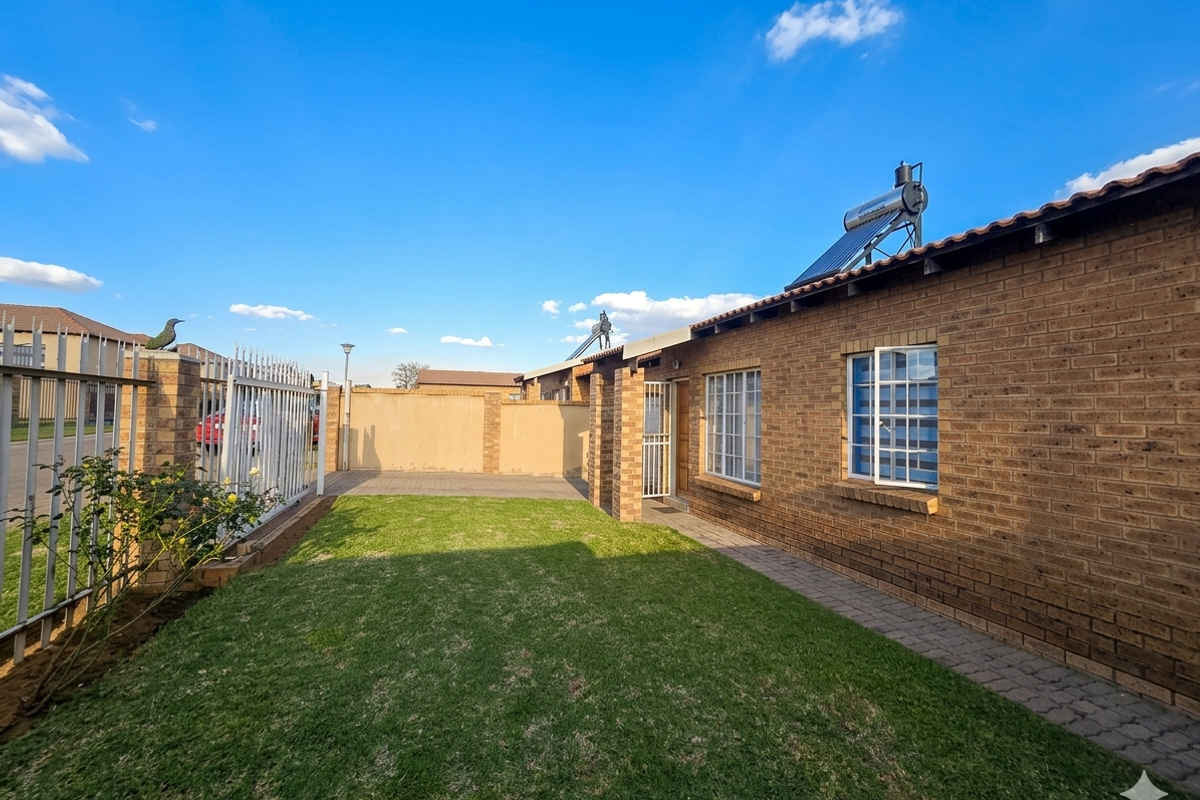 A well-maintained rear exterior view featuring a face brick facade, a neat lawn, paved walkway, and an installed solar water heating system.
