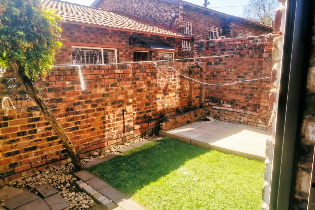 A private rear courtyard featuring a small lawn, paved patio area, and face brick boundary walls, offering a low-maintenance outdoor space.