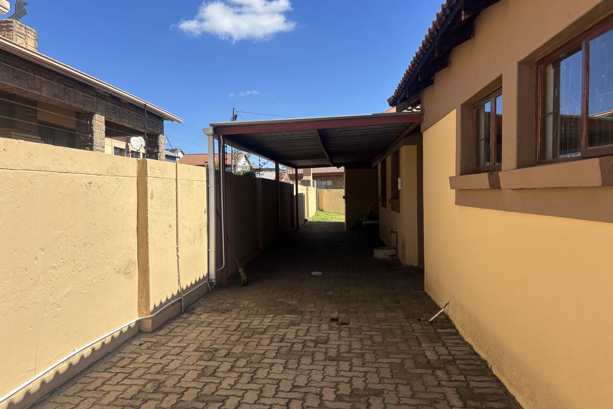 A paved side driveway featuring a covered carport structure and perimeter boundary walls, providing functional outdoor space and vehicle shelter.