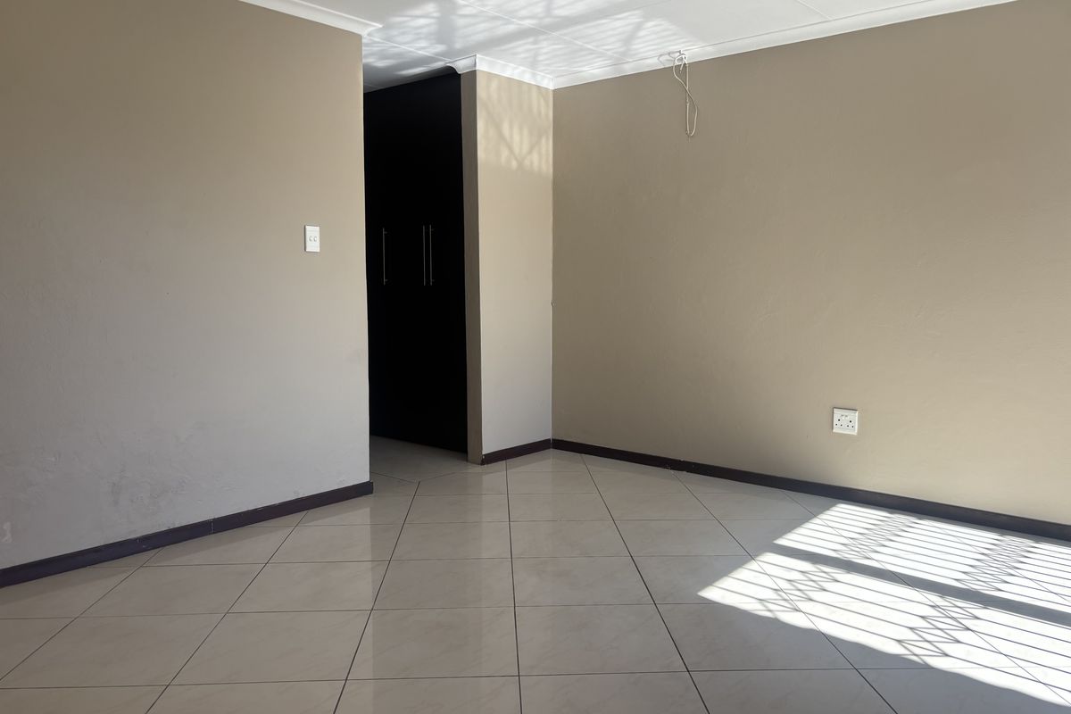 An empty bedroom featuring neutral walls, tiled flooring, and built-in cupboards, with natural light entering through a security-gated window.